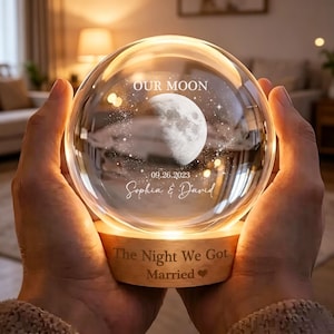 May include: A spherical glass night light featuring an etched moon, the text OUR MOON, the date 09.26.2023, and the names Sophia & David. The wooden base is engraved with the text The Night We Got Married and a heart symbol.