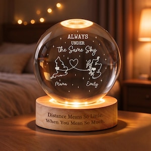 Op de afbeelding: Een heldere glazen bolvormige lamp op een ronde houten voet. De bol bevat gegraveerde kaarten van Engeland en Schotland verbonden door een stippellijn met een hartje, de tekst "ALWAYS UNDER the Same Sky", "Mama" en "Emily". De voet bevat de tekst "Distance Means So Little. When You Mean So Much."