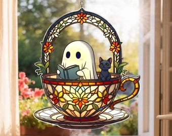 May include: Stained glass window hanging featuring a ghost reading a book inside a teacup with a black cat. The teacup and arch are decorated with colorful floral patterns. A chain is attached for hanging.