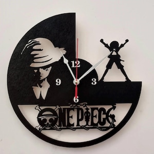 Può includere: Orologio da parete nero con la silhouette di un personaggio con un cappello e un'altra figura con le braccia alzate. L'orologio ha una lancetta dei secondi rossa e la scritta "ONE PIECE" con un teschio e ossa incrociate.