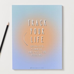 Puede incluir: Un cuaderno con un fondo degradado azul y naranja, con el texto "TRACK YOUR LIFE" y las palabras "CHECKLISTS, PLANNERS, AND PAGES FOR DOODLING". Un lápiz negro con una férula dorada descansa a la izquierda. El cuaderno es para planificar y escribir.