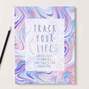 Puede incluir: Un cuaderno con un patrón arremolinado colorido en tonos de rosa, azul y morado. La portada presenta el texto "TRACK YOUR LIFE" con las palabras "CHECKLISTS, PLANNERS, AND PAGES FOR DOODLING" debajo. Un lápiz negro con una virola dorada descansa sobre la superficie blanca.