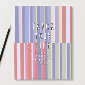 Puede incluir: Un cuaderno con una cubierta a rayas en tonos pastel de rosa, azul y amarillo. El texto "TRACK YOUR LIFE" se muestra de forma destacada, con el subtítulo "CHECKLISTS, PLANNERS, AND PAGES FOR DOODLING". Un lápiz negro con punta dorada descansa junto al cuaderno.