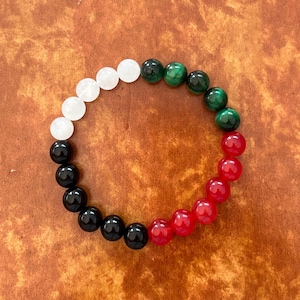 May include: A bracelet made of white, green, black and red beads. The beads are round and have a smooth finish.