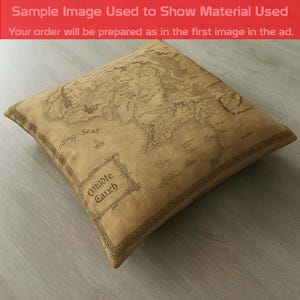May include: Square pillow with a map design in shades of brown. The pillow features a detailed map with text including "Middle Earth" and "Passing Seas". The pillow is on a light gray surface. The text "Sample Image Used to Show Material Used" is visible.