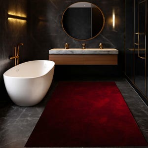 Puede incluir: Un baño moderno con una bañera ovalada blanca, una alfombra roja y una pared de mármol oscuro. El baño cuenta con un tocador de madera con encimera de mármol y un espejo redondo. Los accesorios dorados añaden un toque de lujo.