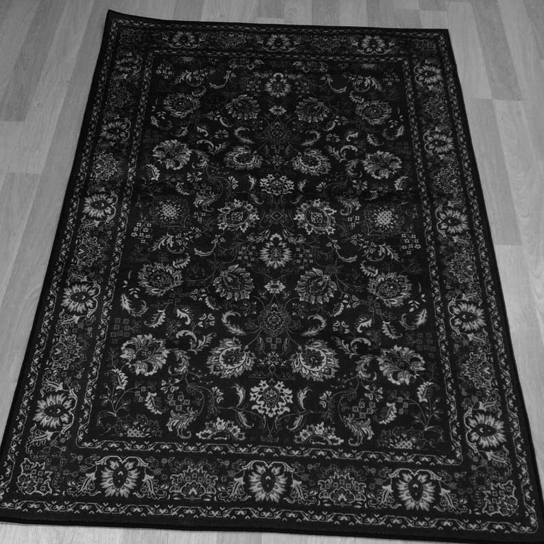 May include: Black and white area rug with an intricate floral pattern. The rug features a dark background with lighter floral and leaf designs throughout. A detailed border frames the central design, creating a classic and elegant look.