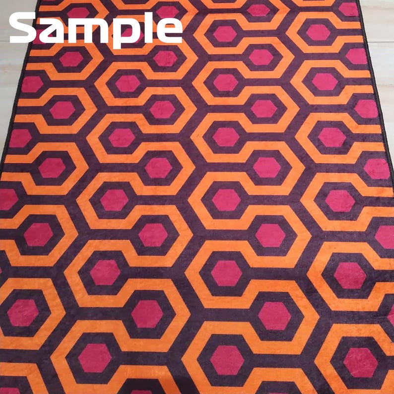 May include: A patterned rug featuring a repeating geometric design in shades of orange, purple, and magenta. The rug's pattern consists of interconnected hexagonal shapes, creating a visually striking and symmetrical pattern. The word "Sample" is printed in white in the upper left corner.