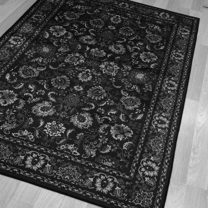 May include: Black and white area rug with a floral pattern. The rug features a dark background with a repeating design of stylized flowers and leaves in lighter shades. A decorative border frames the rug.