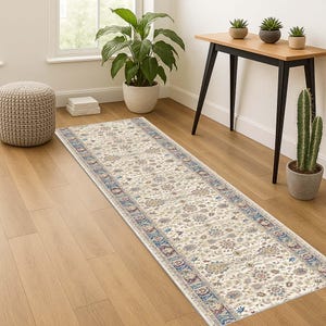 May include: Cream-coloured runner rug featuring a detailed floral design and a blue and burgundy border. The rectangular rug is laid on a wooden floor. This rug is a decorative element for a hallway or entryway.