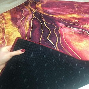 May include: A red and gold area rug with a marbled pattern. The rug has a black backing with a red border.