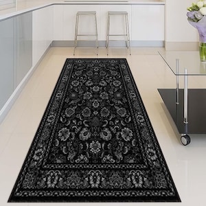 May include: A long, rectangular black rug with a detailed floral pattern. The rug features a dark border and is placed on a light-colored tiled floor. The design includes various floral and leaf motifs.