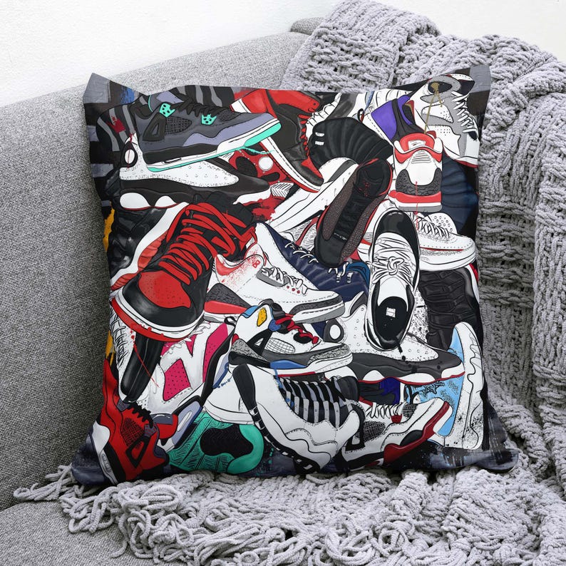 May include: Square throw pillow featuring a collage of colorful sneakers in various styles and colors, including red, black, white, and blue. The pillow is placed on a gray sofa with a matching blanket.