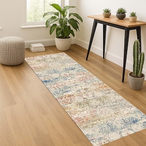 May include: A rectangular area rug with a distressed, vintage-inspired design. The rug features a mix of colors, including cream, blue, red, and green, creating a faded, patterned look. It is placed on a hardwood floor.