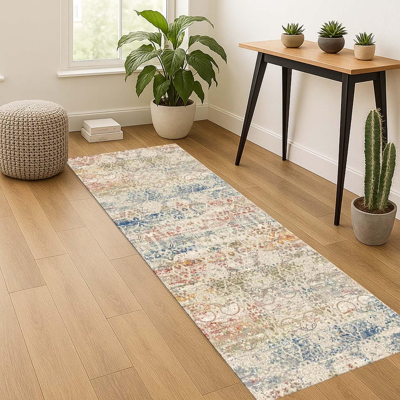May include: A rectangular area rug with a distressed, vintage-inspired design. The rug features a mix of colors, including cream, blue, red, and green, creating a faded, patterned look. It is placed on a hardwood floor.