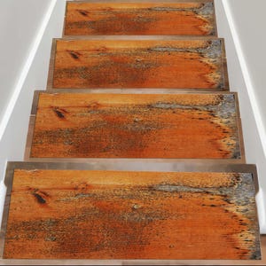 Könnte beinhalten: Treppenstufen mit rustikalem, verwittertem Holz-Aussehen. Die Stufen haben eine warme orangebraune Farbe mit dunkleren Knoten und Maserungsmustern. Die Kanten haben eine metallische Zierleiste, und die Treppe steht vor weißen Wänden.