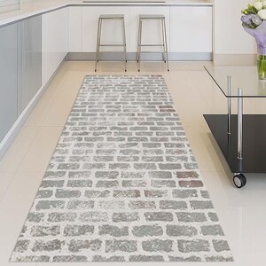 Può includere: Un tappeto rettangolare con motivo a mattoni grigi. Il tappeto è posato su un pavimento piastrellato di colore chiaro. Il design presenta un motivo ripetuto di mattoni rettangolari in tonalità di grigio e un po' di rosso. Il tappeto è in una cucina.