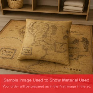 May include: A tan pillow with a map of Middle Earth on top of a matching rug. The rug and pillow have a vintage look. The rug has the words "Middle Earth" and "Mordor" printed on it.