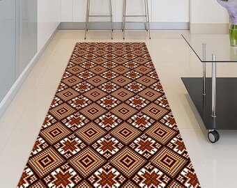 May include: A rectangular runner rug with a geometric pattern in shades of brown, white, and black. The design features repeating diamond and cross-like shapes. The rug is placed on a tiled floor in a kitchen setting.
