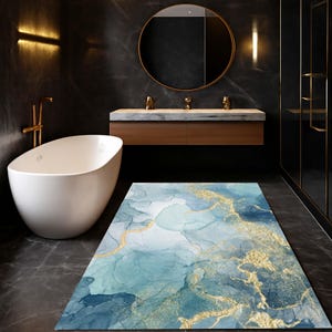 Może przedstawiać: Prostokątny dywanik łazienkowy z abstrakcyjnym niebiesko-złotym wzorem. Dywan ma wzór przypominający akwarelę z odcieniami niebieskiego i złotego, tworząc luksusowy i artystyczny wygląd. Dywanik umieszczony jest w nowoczesnej łazience.