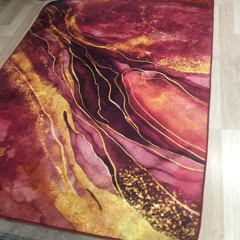 May include: Abstract area rug with a burgundy and gold colour scheme. The rug features a swirling pattern of gold lines on a burgundy background.