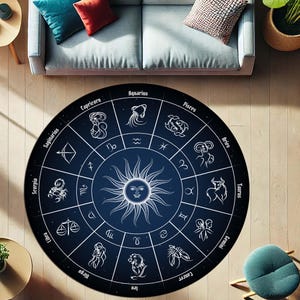 Pode incluir: Tapete redondo com fundo azul escuro com um design de roda do zodíaco branco. A roda inclui símbolos e nomes do zodíaco, com uma ilustração central do sol. O tapete está colocado sobre um chão de madeira, perto de um sofá e cadeiras.