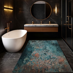 May include: A rectangular bathroom rug with a distressed, mottled design in shades of teal, rust, and dark blue. The rug is placed on a dark gray tiled floor in a modern bathroom setting, with a white bathtub and gold fixtures.