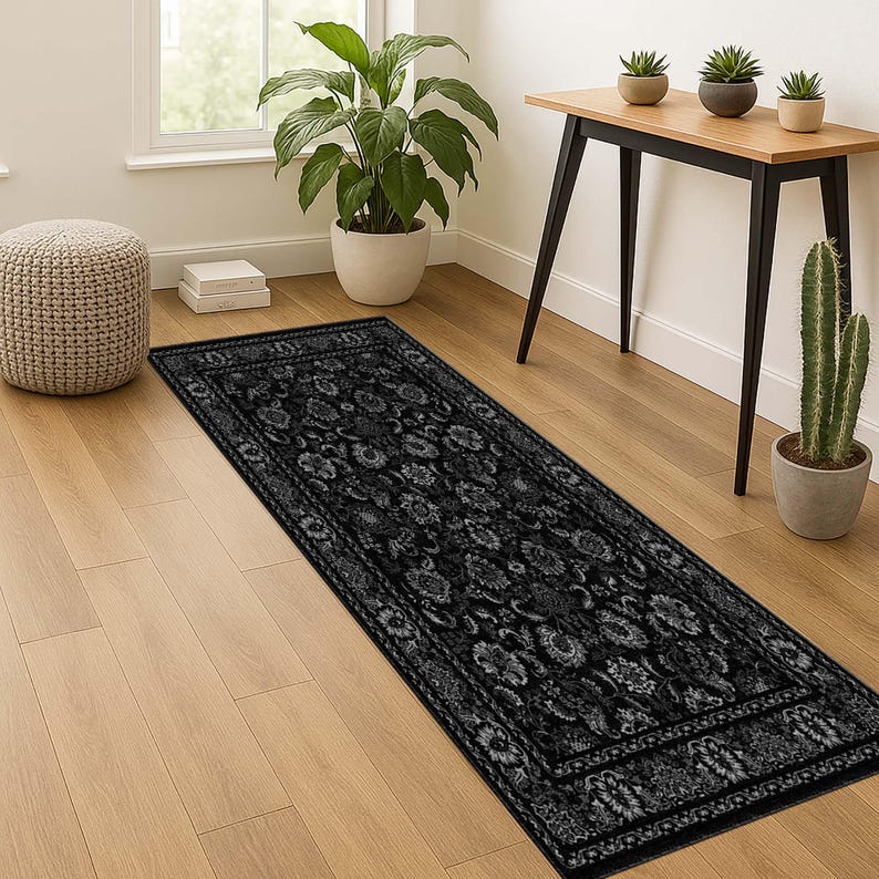 May include: A black and gray floral patterned runner rug. The rug features a detailed design with a border and is placed on a hardwood floor. The rug is rectangular and appears to be made of a soft material.
