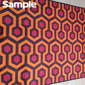 May include: A rectangular rug with a repeating geometric pattern. The design features interconnected orange and dark purple shapes, with magenta hexagon accents. The word "Sample" is printed in white in the upper left corner.