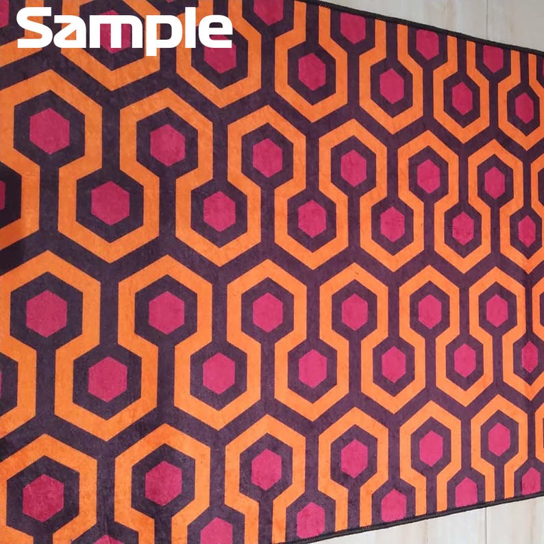 May include: A rectangular rug with a repeating geometric pattern. The design features interconnected orange and dark purple shapes, with magenta hexagon accents. The word "Sample" is printed in white in the upper left corner.