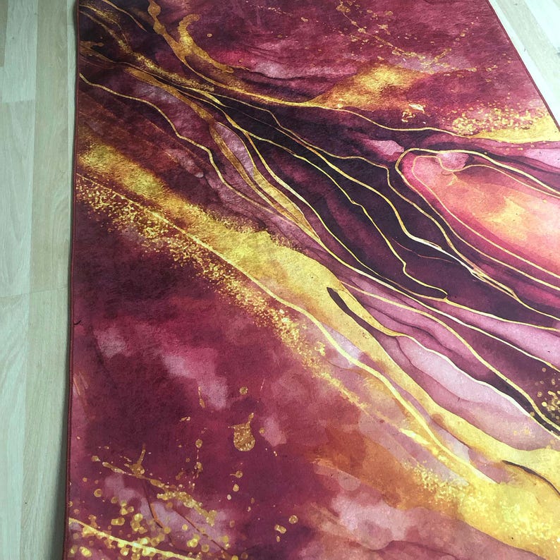 May include: Abstract art rug with a burgundy and gold colour scheme. The rug features a swirling pattern of gold lines on a burgundy background.
