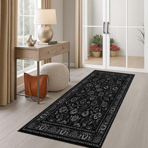 May include: A black floral runner rug with a detailed pattern. The rug is rectangular and placed on a light wood floor. The rug is in a hallway with a table, lamp, and a leather tote bag.