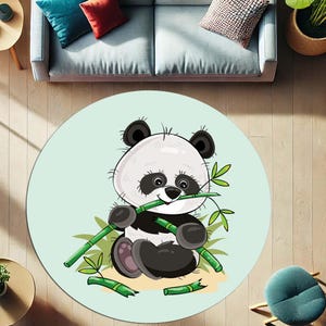 Op de afbeelding: Rond vloerkleed met een cartoon panda die bamboe eet. De panda is zwart en wit met een lichtgroene achtergrond. Een zacht, decoratief accent voor een kinderkamer of woonkamer.