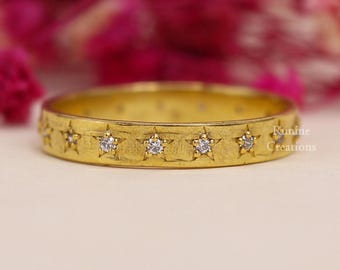 Op de afbeelding: Een gouden bandring met een geborstelde afwerking en kleine diamanten die in stervormen rond de band zijn gezet.