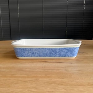 Könnte beinhalten: Rechteckige Keramik-Backform mit weißem Innenraum und blau gemusterter Außenseite. Das blaue Muster hat einen Marmoreffekt und die Form hat kleine Griffe an jedem Ende. Dekorativer Küchenartikel.