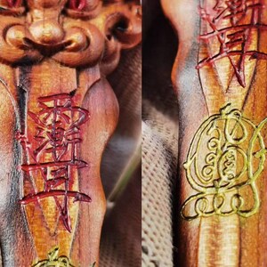 May include: Close-up of a carved wooden object with intricate details. The object features red and gold painted Chinese characters and symbols. The wood has a warm, natural tone with visible grain.