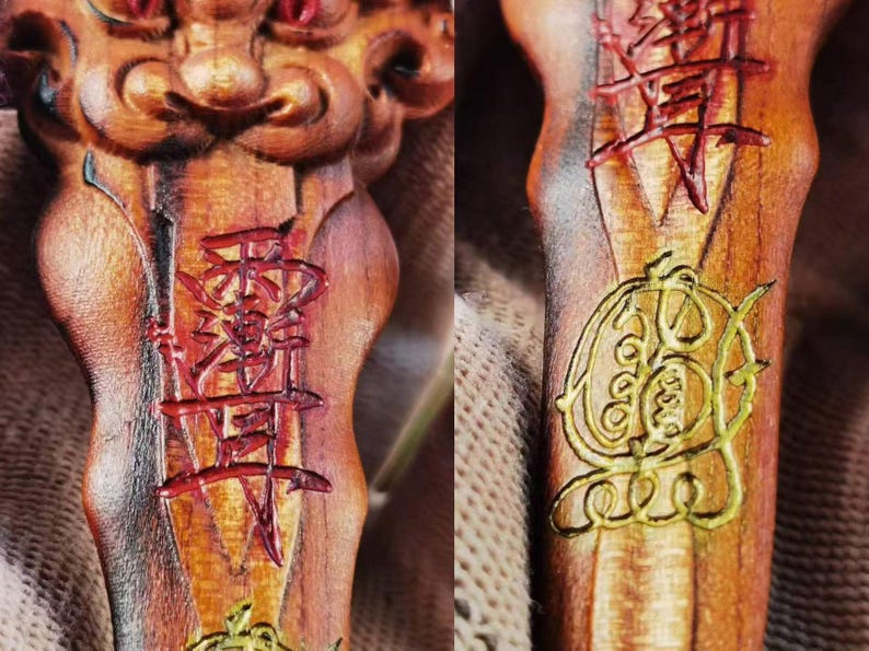 May include: Close-up of a carved wooden object with intricate details. The object features red and gold painted Chinese characters and symbols. The wood has a warm, natural tone with visible grain.
