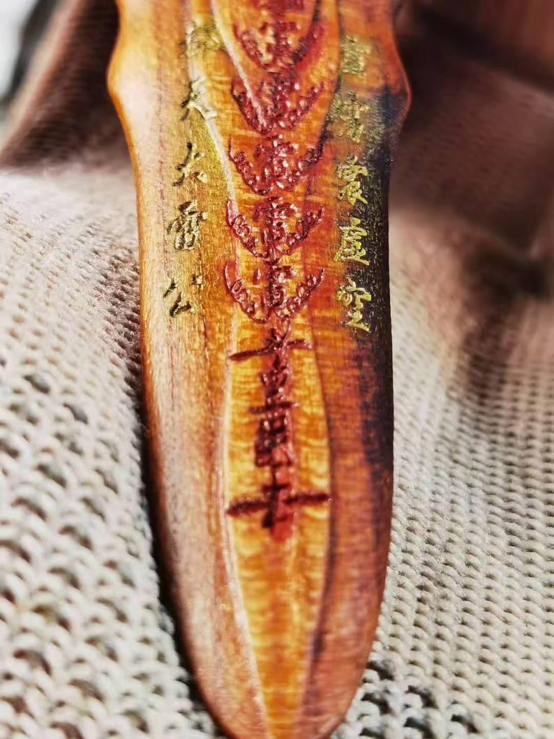 May include: Close-up of a wooden object with intricate carvings and inscriptions in gold and red. The wood has a warm, reddish-brown hue with visible grain. The carvings appear to be of a religious or cultural nature, with detailed patterns and symbols.