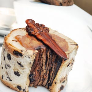 May include: A wooden log cake with a brown wooden carving on top. The cake is on a white plate.