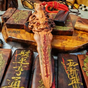 May include: Wooden carvings and pendants with gold-colored Chinese characters and illustrations. A central, intricately carved wooden figure with a face and red accents is the focal point. Other wooden pieces are rectangular with gold designs.