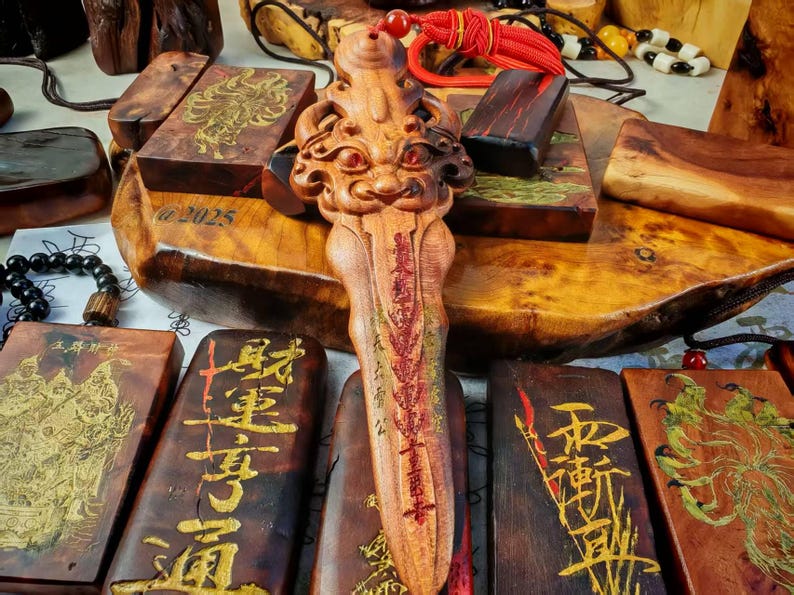 May include: Wooden carvings and pendants with gold-colored Chinese characters and illustrations. A central, intricately carved wooden figure with a face and red accents is the focal point. Other wooden pieces are rectangular with gold designs.
