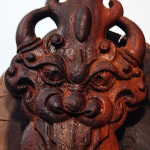 May include: A dark brown wooden carving of a mythical creature with intricate details. The creature has a fierce expression with large eyes and a wide mouth. The carving is a traditional art form and would make a unique decorative piece.