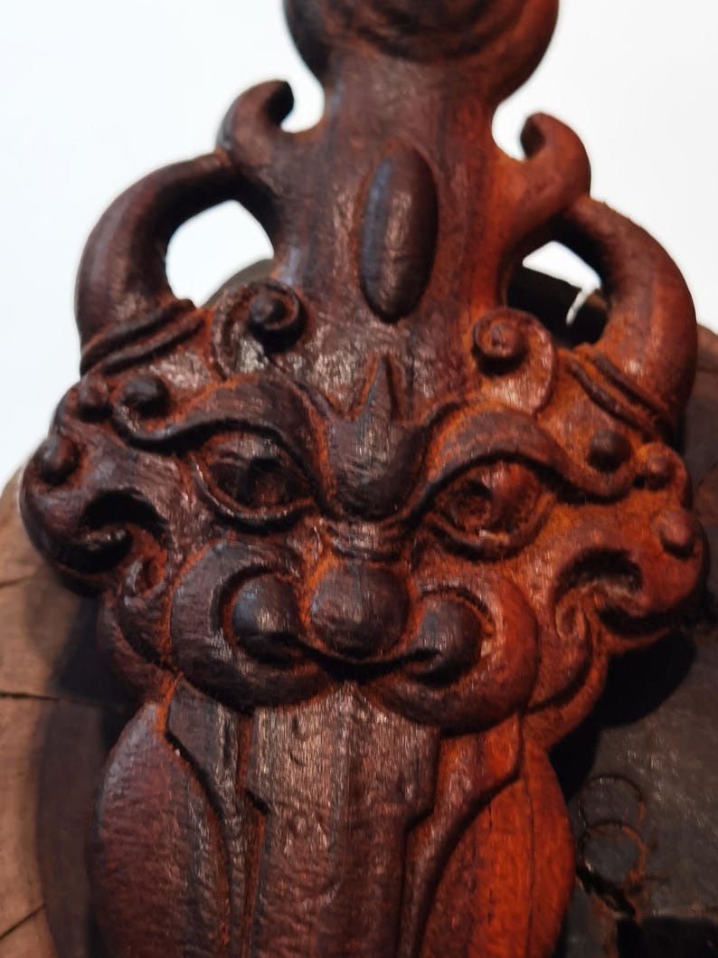 May include: A dark brown wooden carving of a mythical creature with intricate details. The creature has a fierce expression with large eyes and a wide mouth. The carving is a traditional art form and would make a unique decorative piece.