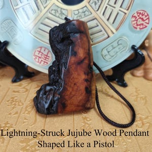 May include: A jujube wood pendant, shaped like a pistol, with a dark brown cord. The pendant is a mix of dark and light brown colors. The text on the image reads "Lightning-Struck Jujube Wood Pendant Shaped Like a Pistol."