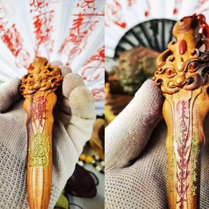 May include: A carved wooden decorative item with intricate details. The item features a detailed carving at the top and is adorned with red and gold accents. The item has Chinese characters and symbols carved into the wood.