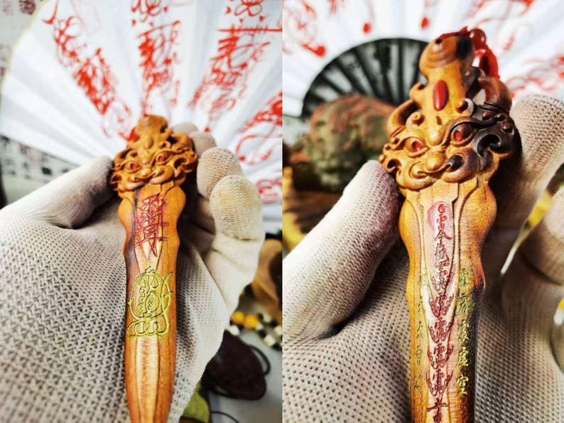 May include: A carved wooden decorative item with intricate details. The item features a detailed carving at the top and is adorned with red and gold accents. The item has Chinese characters and symbols carved into the wood.