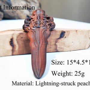 May include: A wooden carving in the shape of a dagger with intricate details. The carving is made from lightning-struck peach wood and measures 15 inches by 4.5 inches by 1 inch. It weighs 25 grams.