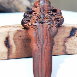 May include: A hand-carved wooden sword pendant with intricate details and a dark brown finish.