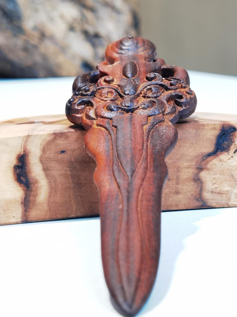 May include: A hand-carved wooden sword pendant with intricate details and a dark brown finish.
