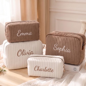 May include: Four rectangular cosmetic bags with a vertical ribbed texture and zippered closures. Two bags are brown with white embroidered names Emma and Sophia, and two are white with brown embroidered names Olivia and Charlotte.